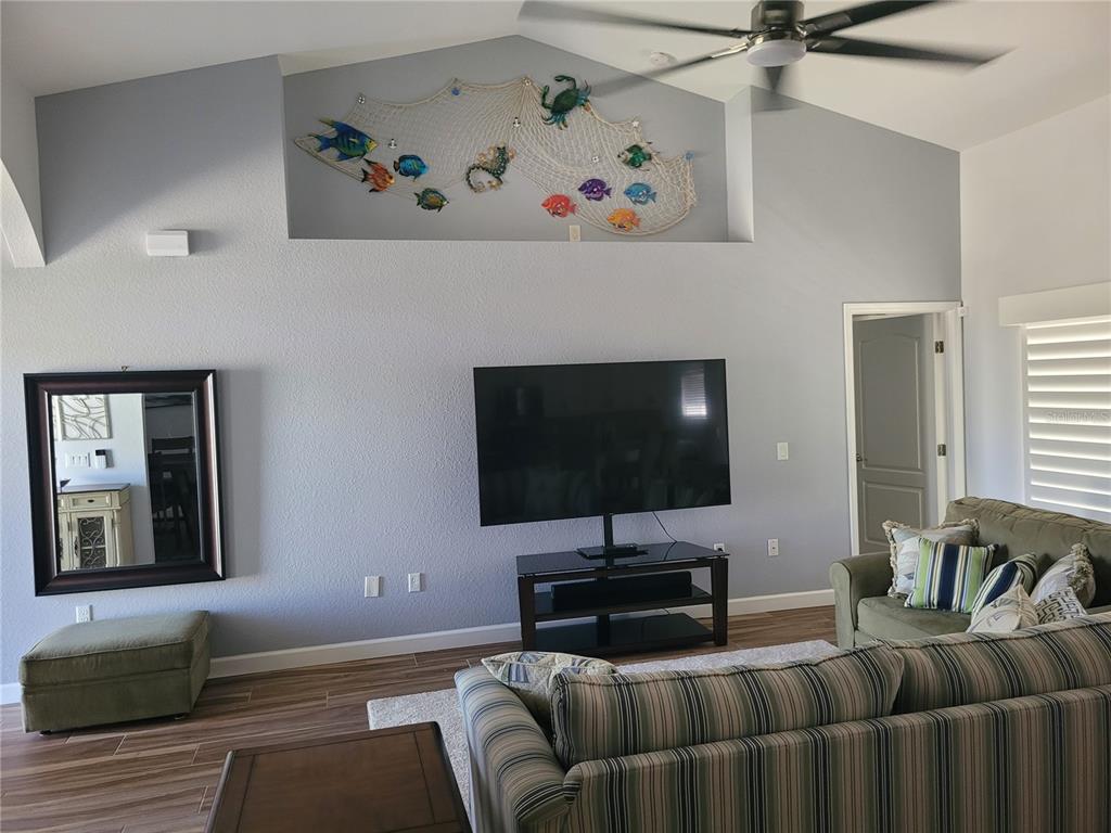 A living room features a vaulted ceiling, a wall-mounted television, and a decorative fishing net — 5530 ALMAR DRIVE, PUNTA GORDA, FL