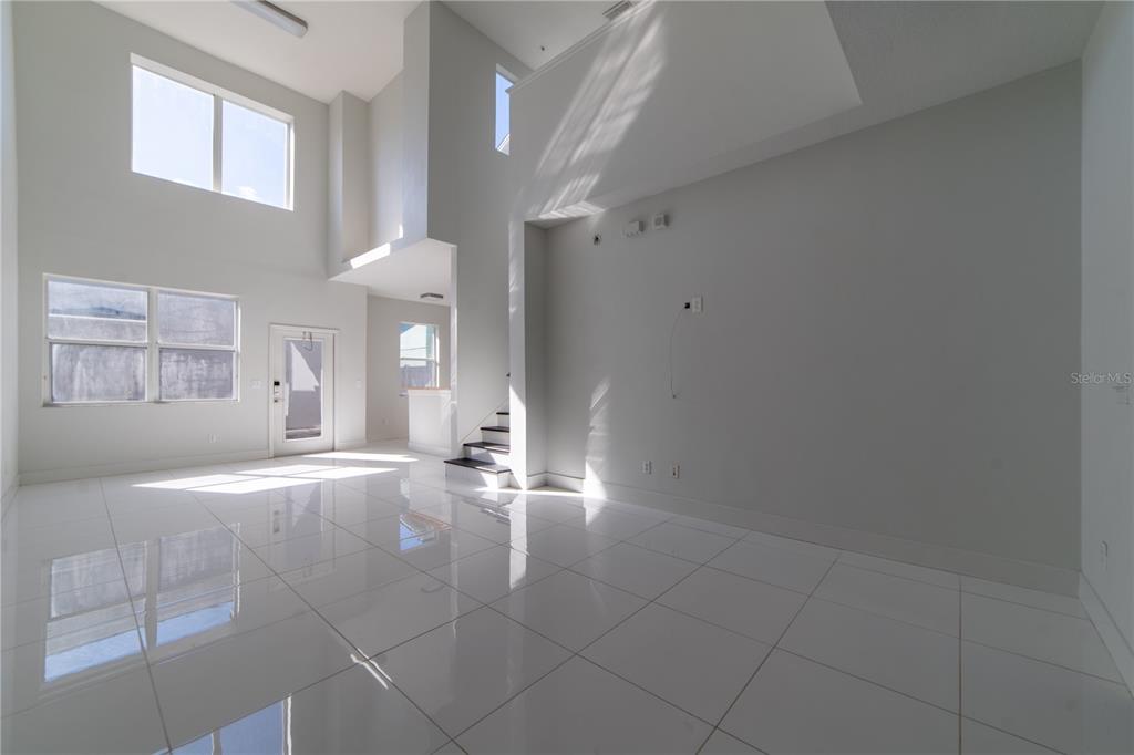 A bright, empty living room features high ceilings, white tile flooring, and a staircase — 10224 VICKERS RIDGE DRIVE UNIT 10224, ORLANDO, FL
