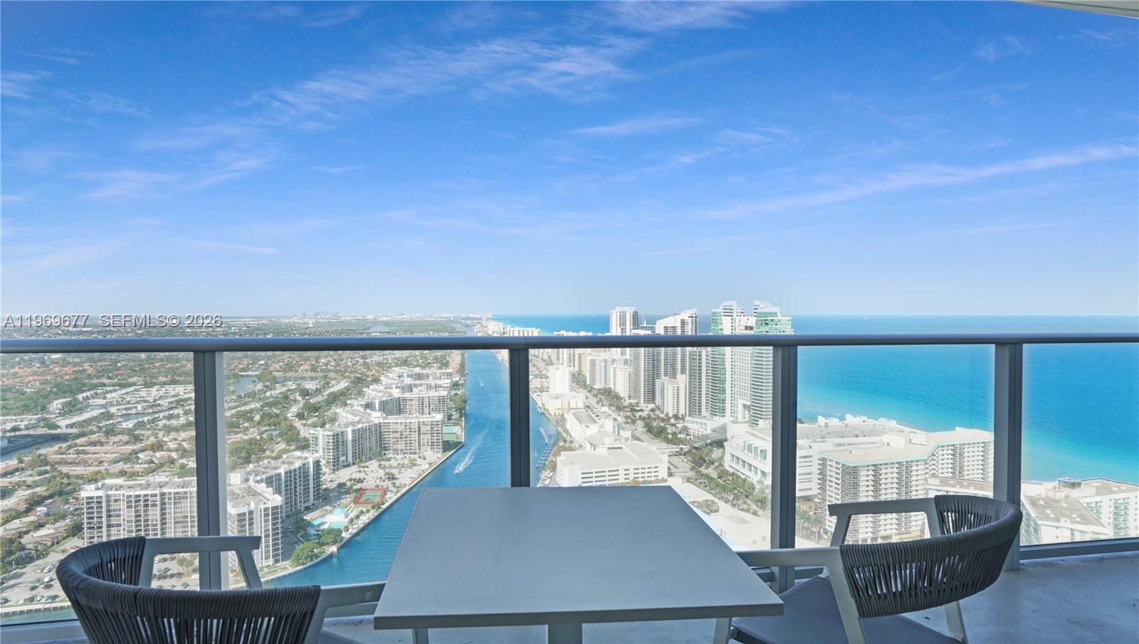 A high-rise balcony features a table and chairs overlooking a coastal city and ocean — 4010 S Ocean Dr # T4002, Hollywood FL 33019, HOLLYWOOD, FL