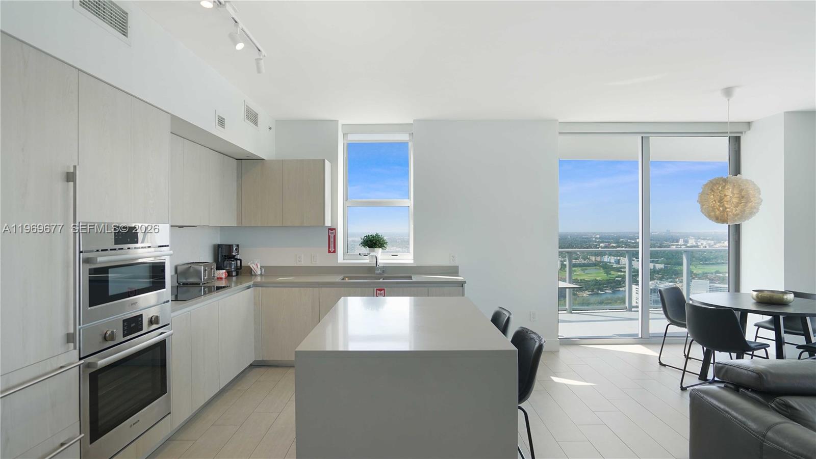 A modern kitchen features light wood cabinetry, a central island, and floor-to-ceiling windows with views — 4010 S Ocean Dr # T4002, Hollywood FL 33019, HOLLYWOOD, FL