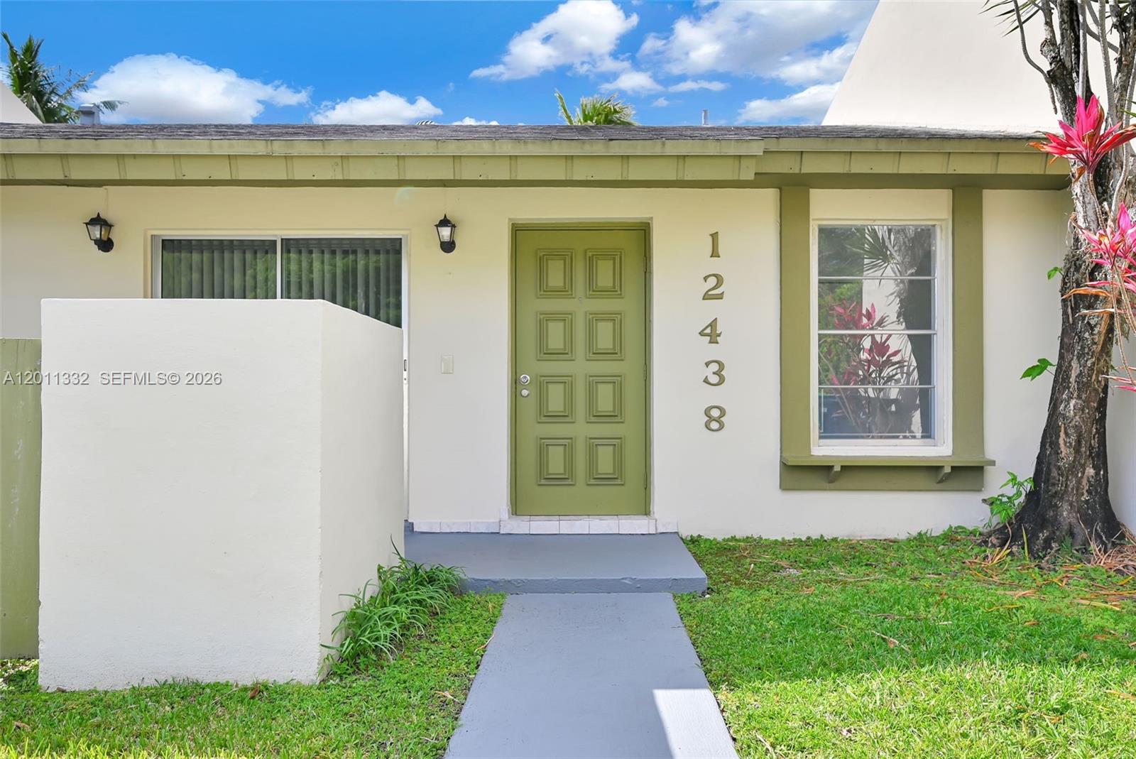 The exterior of a single-story house features a green door, a walkway, and a window — 12438 SW 115th Ter, Miami FL 33186, MIAMI, FL