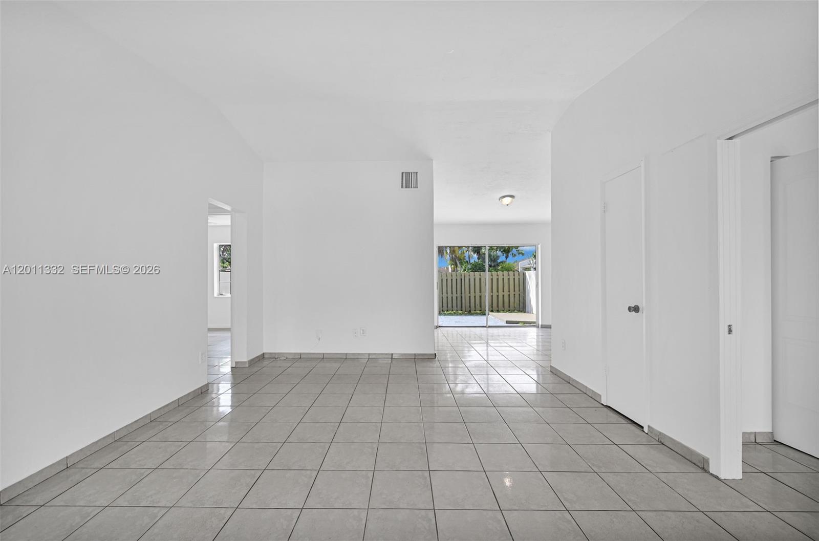 A bright, empty room features white walls, light-colored floor tiles, and a sliding glass door — 12438 SW 115th Ter, Miami FL 33186, MIAMI, FL