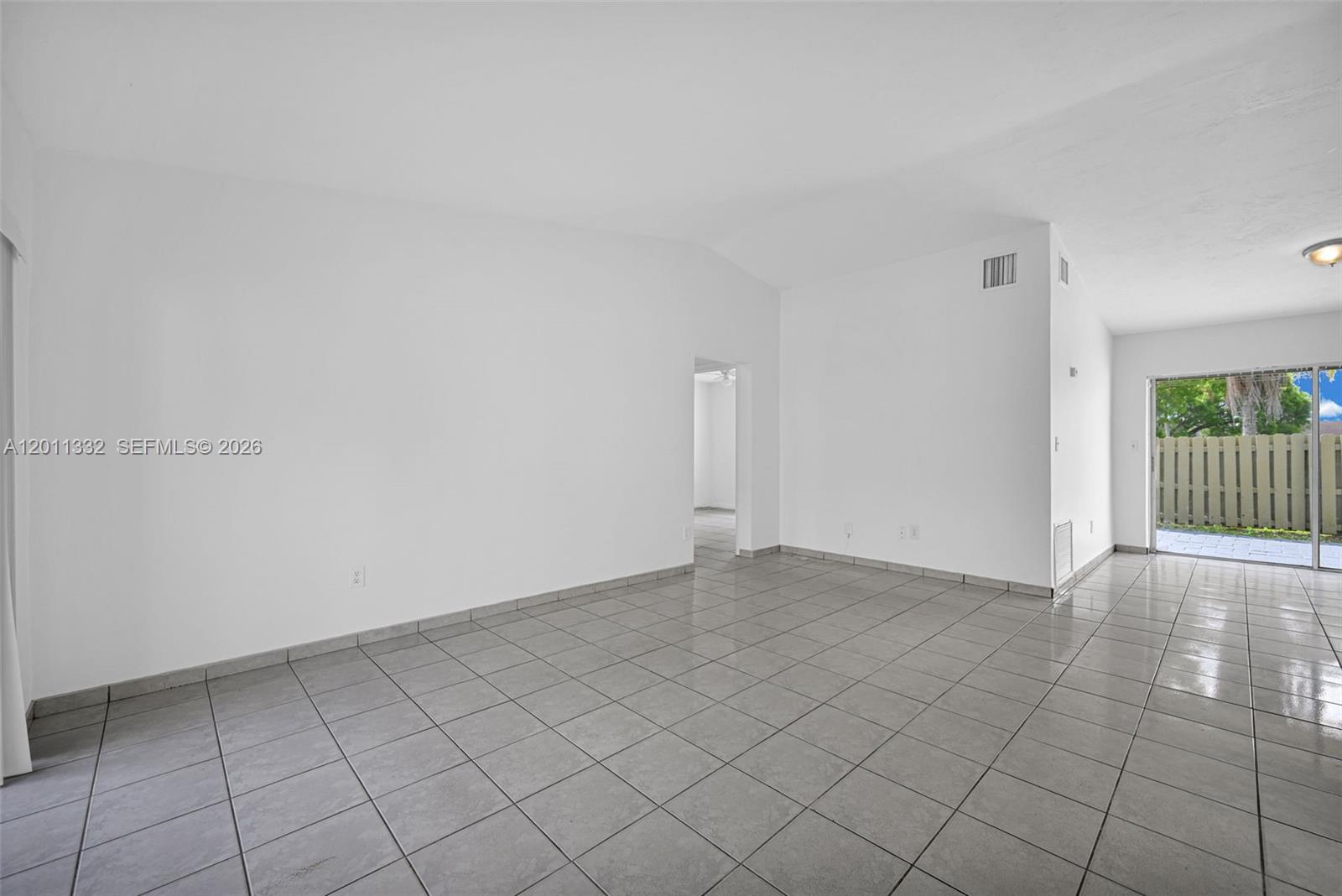 An empty room features white walls, gray tile flooring, and a sliding glass door — 12438 SW 115th Ter, Miami FL 33186, MIAMI, FL