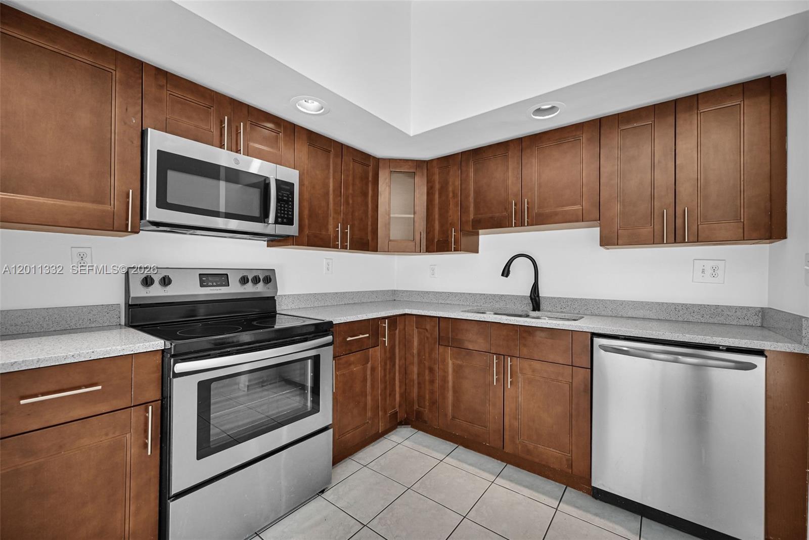 A kitchen features brown wooden cabinets, stainless steel appliances, and light-colored granite countertops — 12438 SW 115th Ter, Miami FL 33186, MIAMI, FL