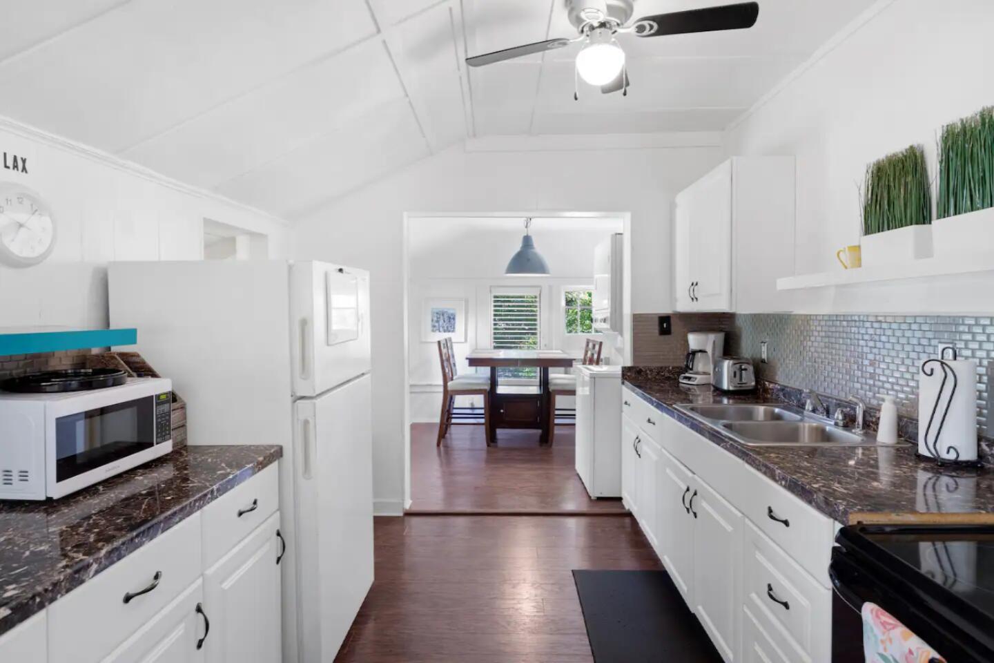 A white kitchen with dark marble countertops leads into a dining area with wood floors — 204 S M Street, FL 33460, FL
