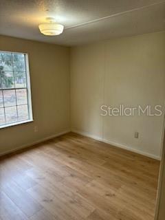 An empty bedroom features light wood-look flooring, beige walls, and a single window — 175 PIEDMONT COURT, MELROSE, FL