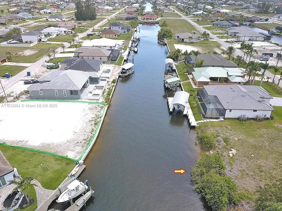 An aerial view shows a canal lined with residential houses, boat docks, and boat lifts — 1253 NW 39th Ave, Cape Coral FL 33993, CAPE CORAL, FL