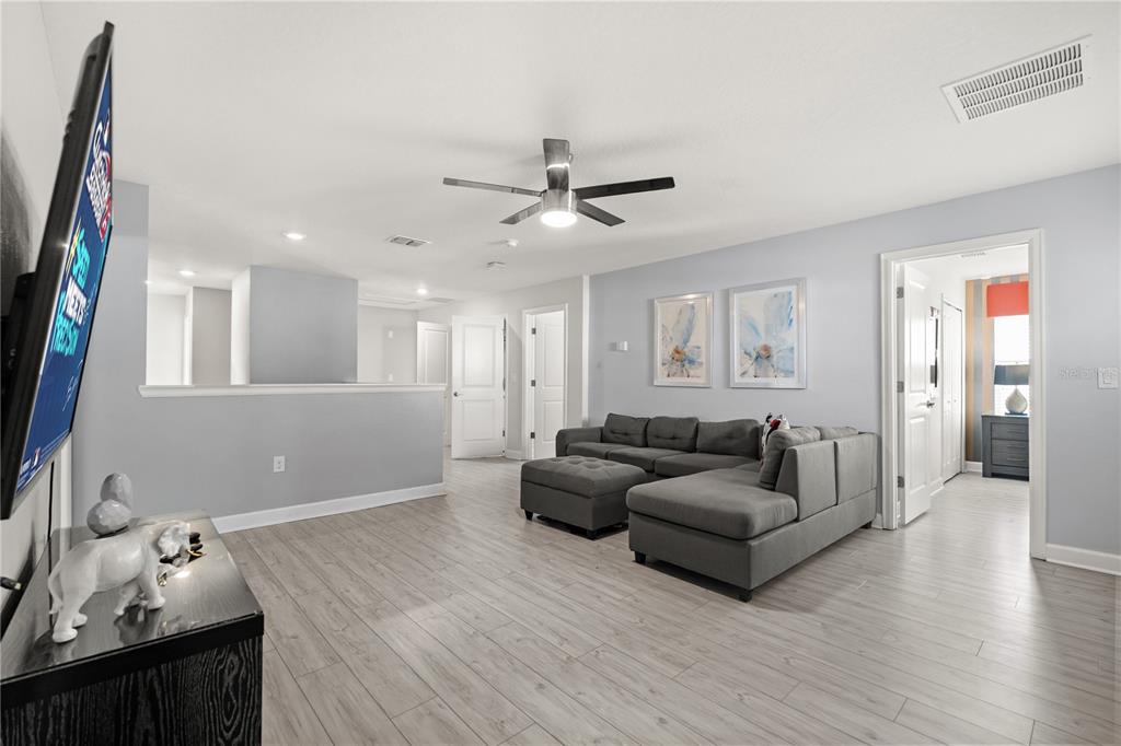 A living room features light wood-look flooring, a gray sectional sofa, and a ceiling fan — 1592 MAIDSTONE COURT, DAVENPORT, FL