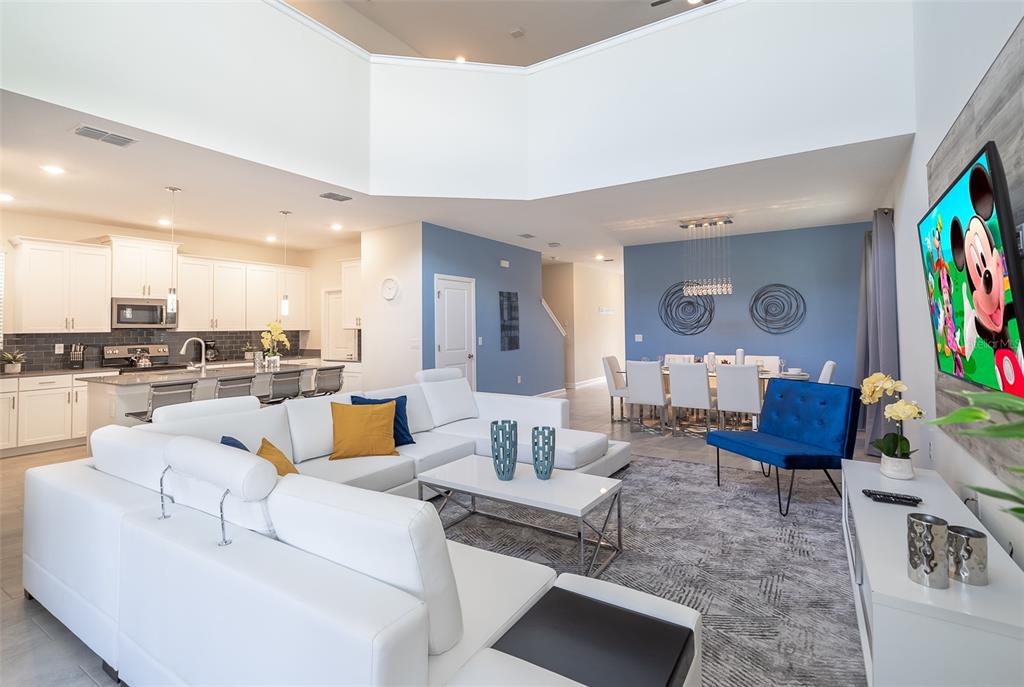 An open-concept living room and kitchen feature white cabinetry, a sectional sofa, and blue accents — 2764 BOOKMARK DRIVE, KISSIMMEE, FL