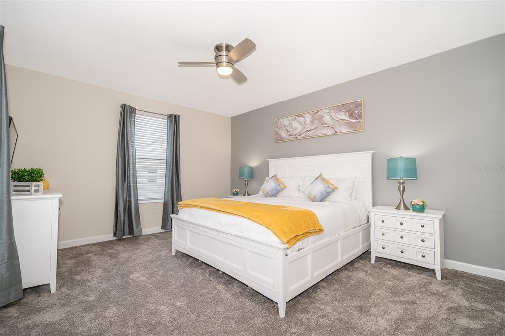 A bedroom features a white bed, gray carpet, a ceiling fan, and two nightstands — 2764 BOOKMARK DRIVE, KISSIMMEE, FL