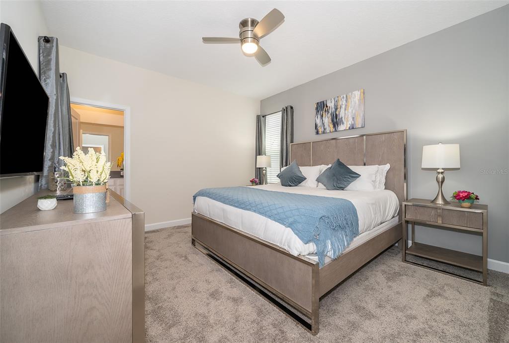 A bedroom features a king-sized bed with a blue throw, gray carpet, and a ceiling fan — 2764 BOOKMARK DRIVE, KISSIMMEE, FL