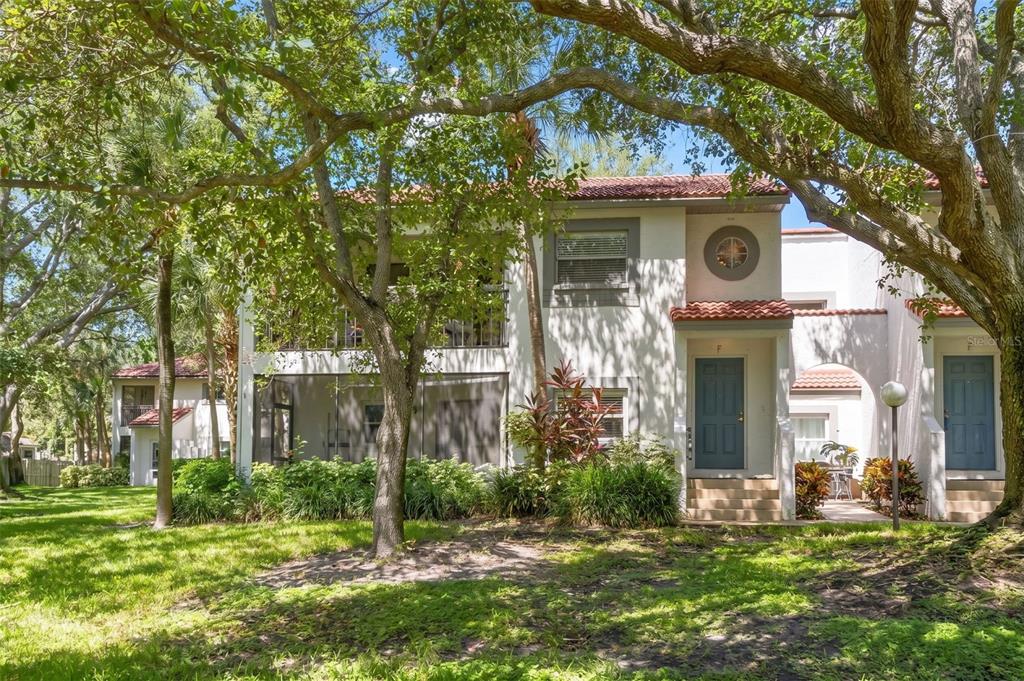 A two-story stucco townhouse with a screened balcony, tiled roof, and blue front doors — 500 SANTA CRUZ PLACE NE UNIT F, ST PETERSBURG, FL
