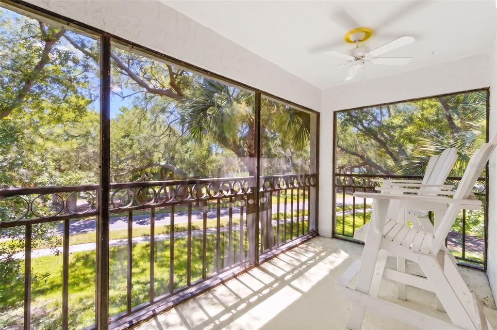 A screened-in balcony features white Adirondack chairs, a ceiling fan, and views of trees outside — 500 SANTA CRUZ PLACE NE UNIT F, ST PETERSBURG, FL