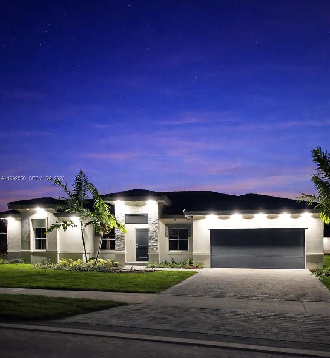 A single-story house with a stone-accented entryway, garage, and exterior lighting at twilight — 19303 SW 132nd Path, Miami FL 33177, MIAMI, FL