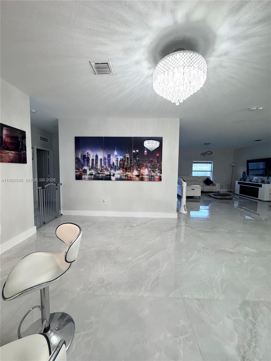 A bright, open-concept living area features white tile flooring, a crystal chandelier, and city-themed art — 19303 SW 132nd Path, Miami FL 33177, MIAMI, FL