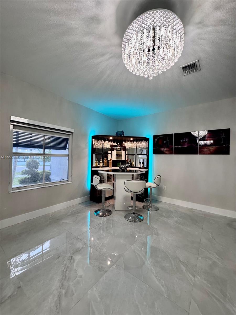 A room with a corner bar, three stools, a crystal chandelier, and gray tile flooring — 19303 SW 132nd Path, Miami FL 33177, MIAMI, FL