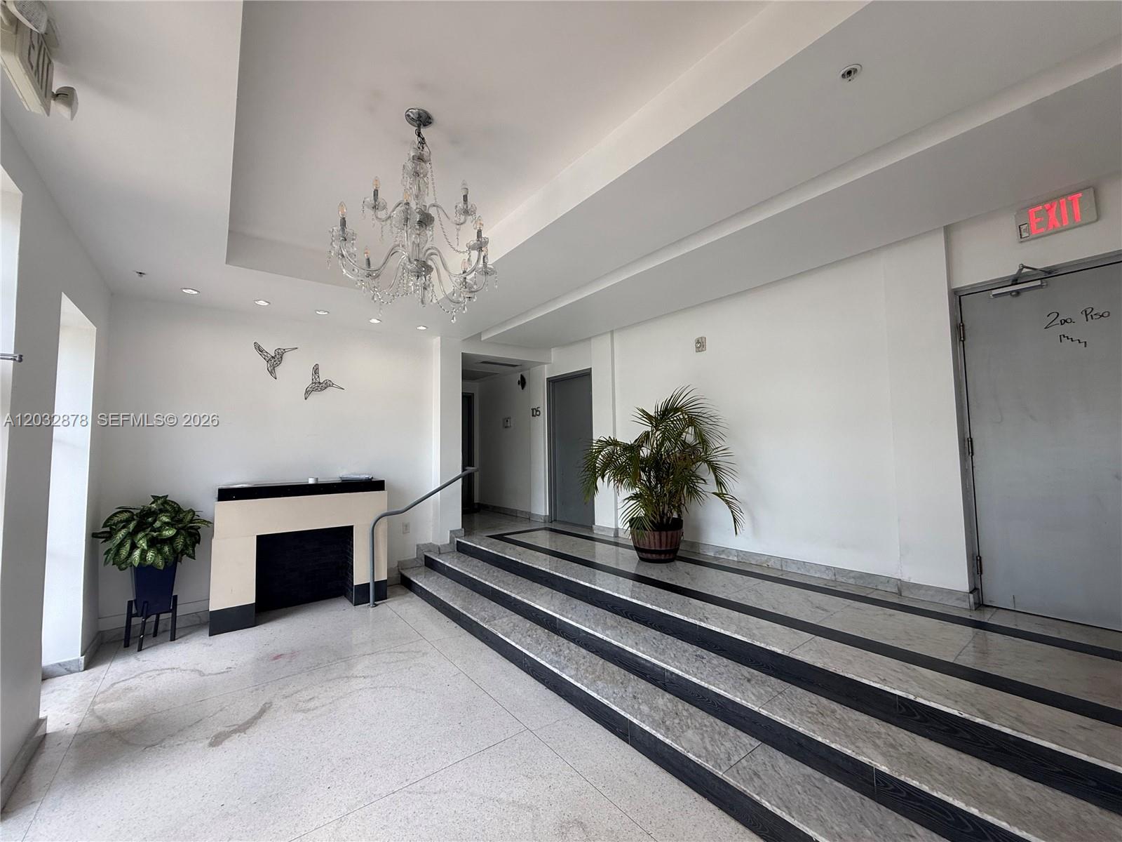 A building lobby features a chandelier, a fireplace, stairs, and a potted plant — 1600 Euclid Ave # 102, Miami Beach FL 33139, MIAMI BEACH, FL