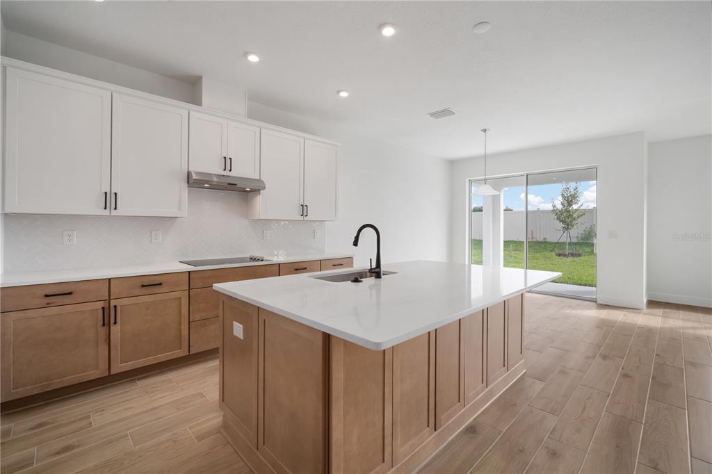 A kitchen features a central island, white upper cabinets, wood lower cabinets, and sliding glass doors — 2951 STEWART CREEK CIRCLE, PLANT CITY, FL