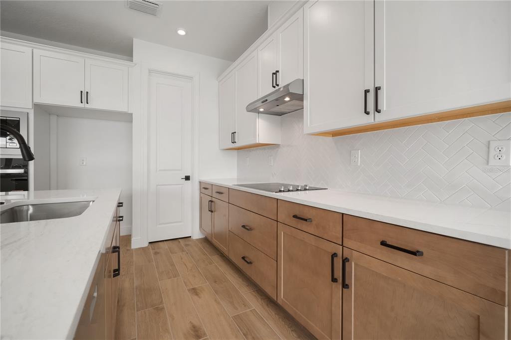 A modern kitchen features two-toned cabinetry, white countertops, and a herringbone-patterned tile backsplash — 2951 STEWART CREEK CIRCLE, PLANT CITY, FL