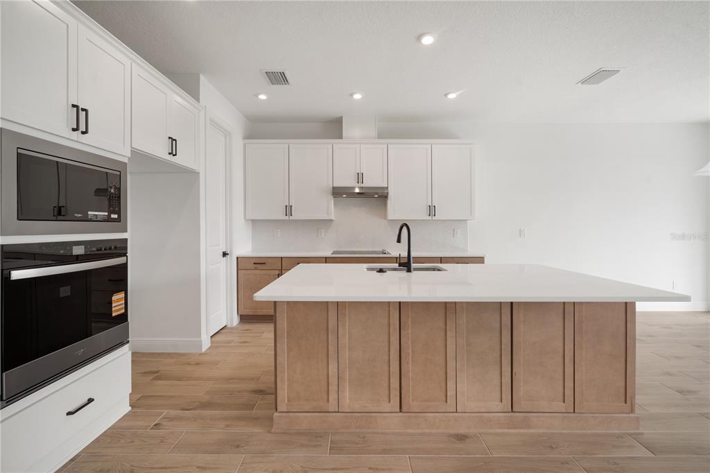 A modern kitchen features white upper cabinets, wood-toned lower cabinets, a large island, and appliances — 2951 STEWART CREEK CIRCLE, PLANT CITY, FL