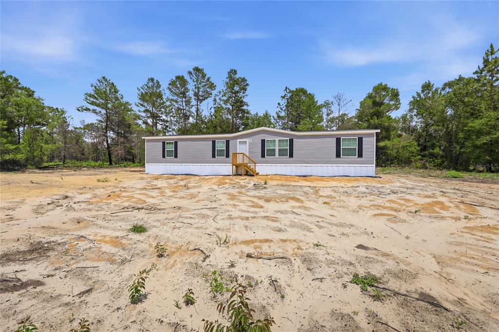 A light gray manufactured home sits on a large, sandy, undeveloped lot with surrounding trees — 150 19TH STREET, INTERLACHEN, FL