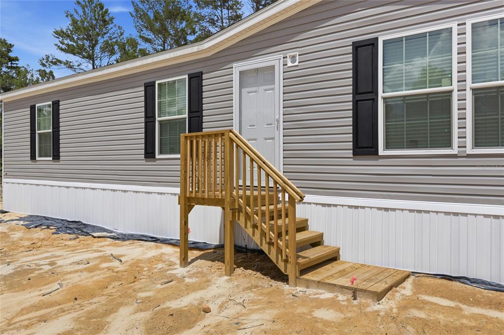 A gray manufactured home exterior features a wooden staircase leading to a white entry door — 150 19TH STREET, INTERLACHEN, FL