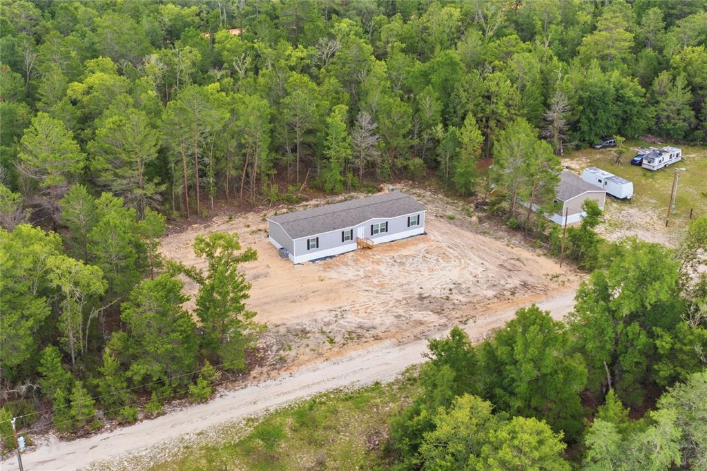 An aerial view shows a manufactured home situated on a cleared lot surrounded by trees — 150 19TH STREET, INTERLACHEN, FL