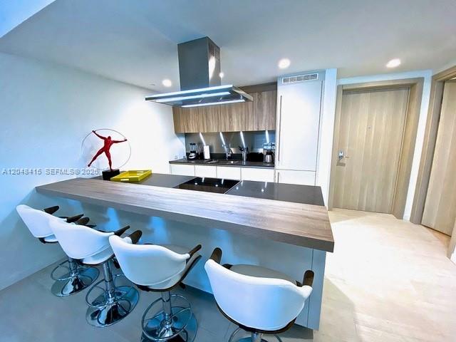 A modern kitchen features a wooden breakfast bar with white stools and stainless steel appliances — 1000 Brickell Plaza # 1914, Miami FL 33131, MIAMI, FL