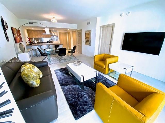 A modern living room features a dark sofa, two yellow armchairs, and an open kitchen — 1000 Brickell Plaza # 1914, Miami FL 33131, MIAMI, FL