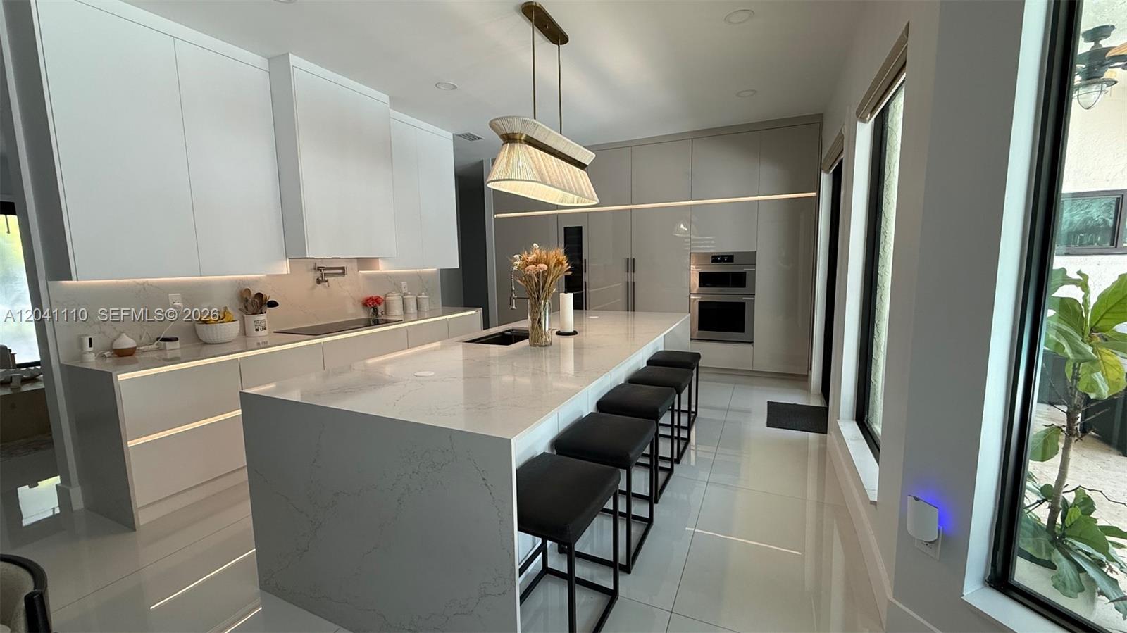 A modern kitchen features a large white quartz island, high-gloss cabinetry, and black bar stools — Cabinet Manufacturing, Hialeah FL 33016, HIALEAH, FL