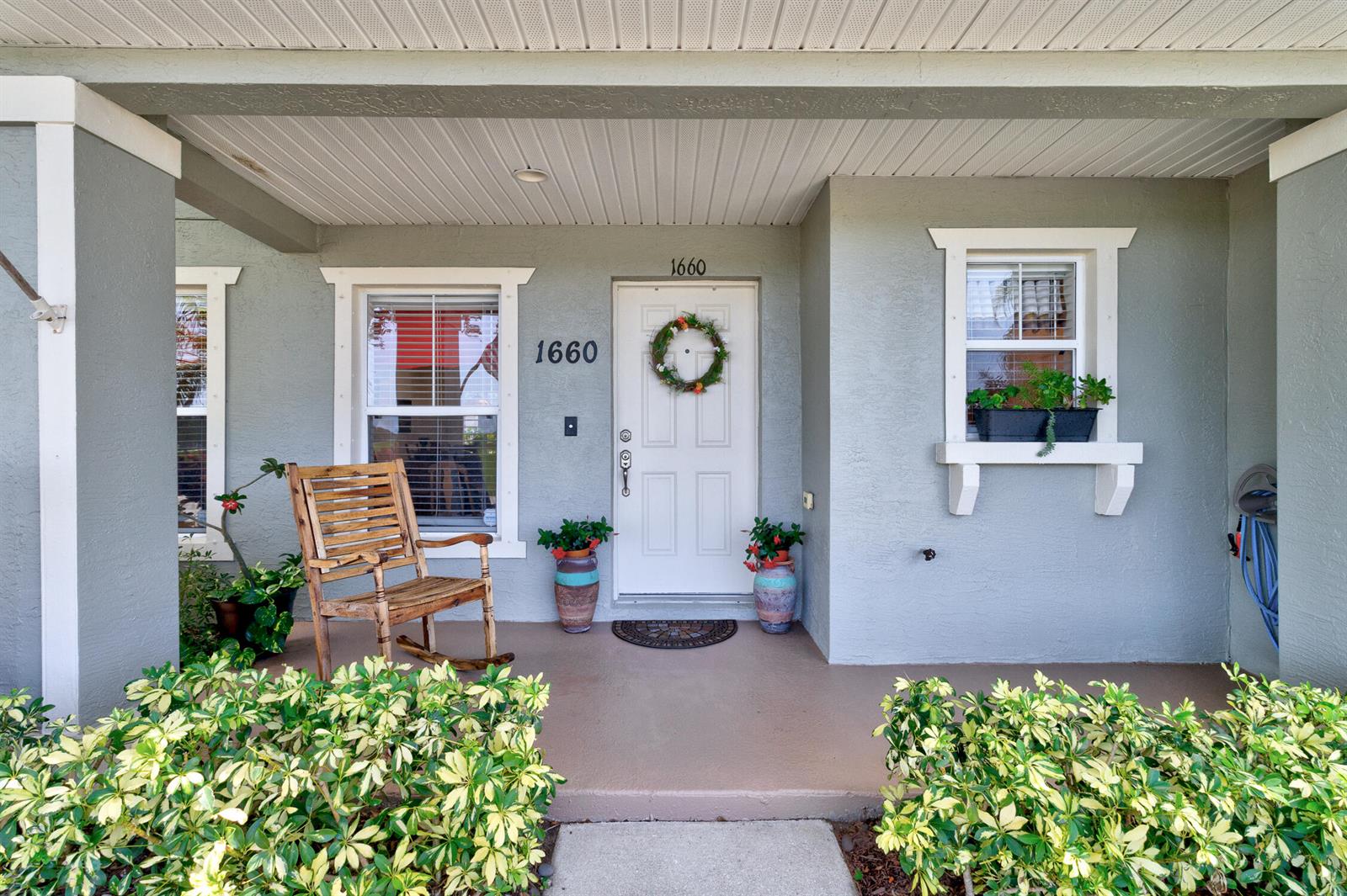 A covered front porch features a wooden rocking chair, potted plants, and a white door — 1660 Pointe W Way, Vero Beach FL 32966, VERO BEACH, FL