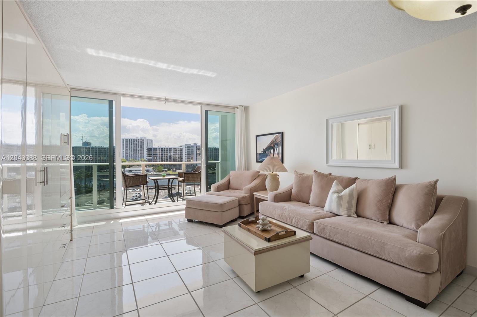 A living room features light-colored tile floors, a beige sofa, and a balcony with water views — 3505 S OCEAN DR # 604, Hollywood FL 33019, HOLLYWOOD, FL