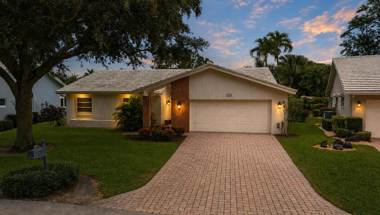 A single-story house with a brick accent wall, light siding, and a paved driveway at dusk — 5557 N Cameo Drive N, Boca Raton FL 33433, BOCA RATON, FL