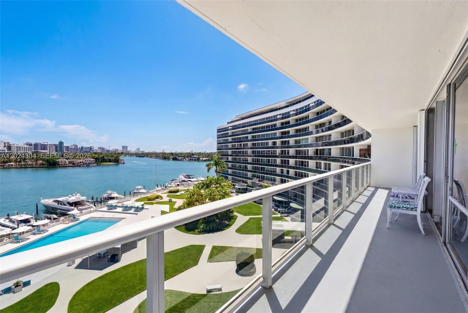 A balcony overlooks a swimming pool, a marina, and a curved apartment building — 900 Bay Dr # 606, Miami Beach FL 33141, MIAMI BEACH, FL