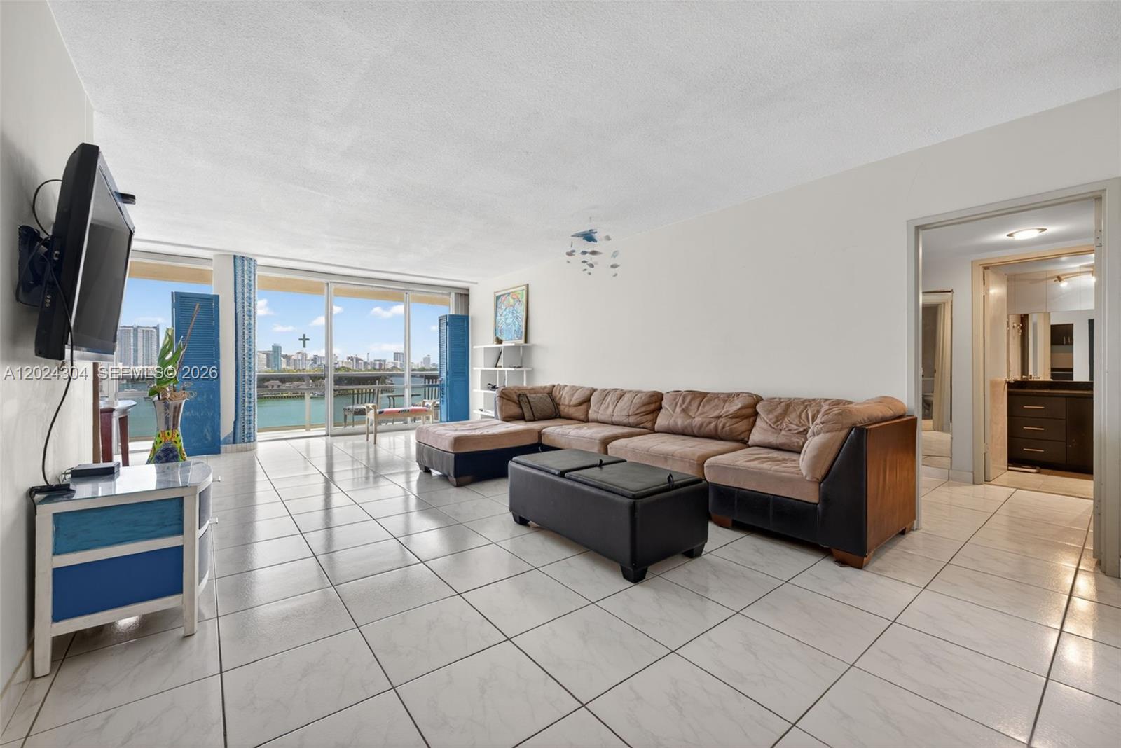 A living room features white tile floors, a large sectional sofa, and a waterfront balcony — 900 Bay Dr # 606, Miami Beach FL 33141, MIAMI BEACH, FL