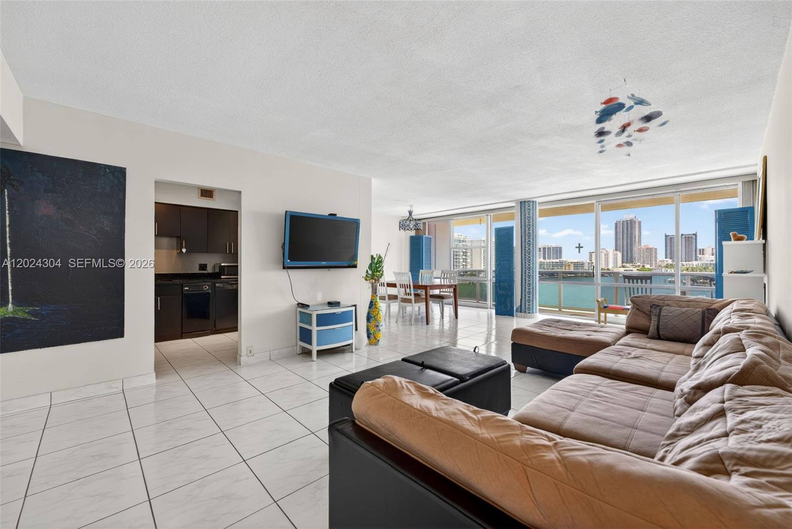A living room with tile floors, a brown sectional, and a view of the city — 900 Bay Dr # 606, Miami Beach FL 33141, MIAMI BEACH, FL