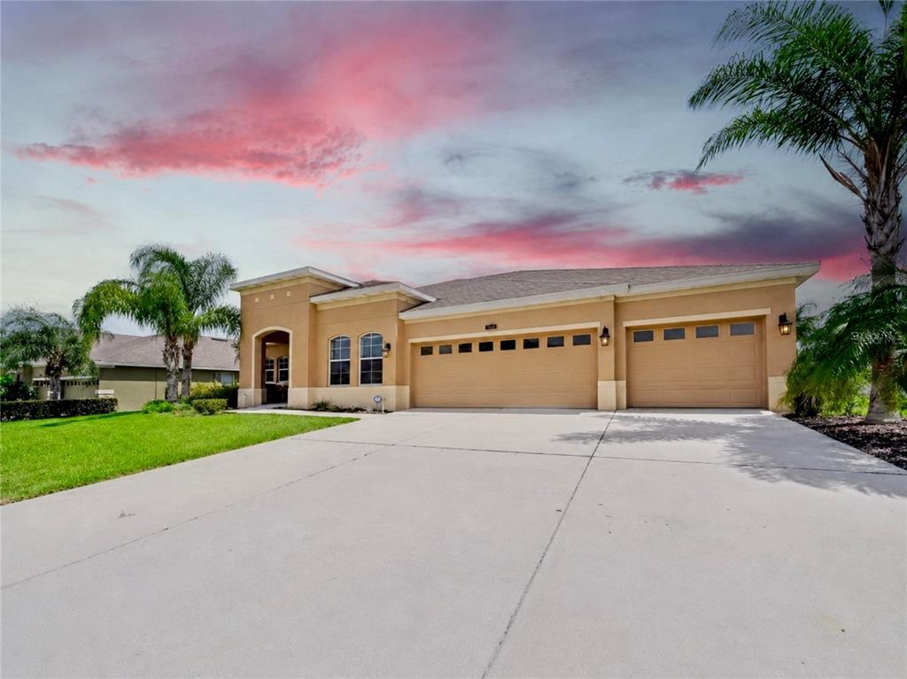 A tan single-story house with a three-car garage and a concrete driveway under a sunset — 428 PALASTRO AVENUE, AUBURNDALE, FL