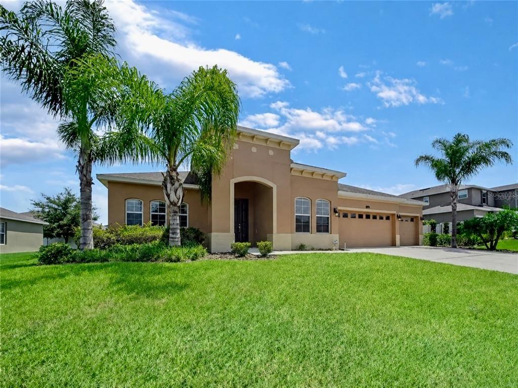 A single-story tan stucco house with a three-car garage and two palm trees in front — 428 PALASTRO AVENUE, AUBURNDALE, FL