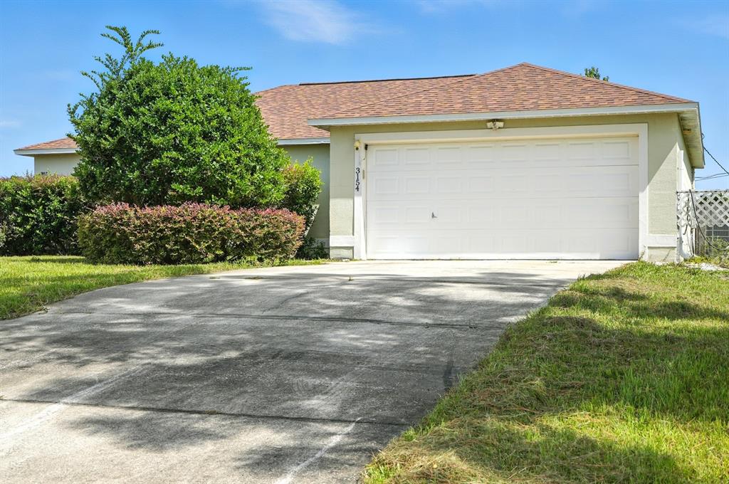 A single-story house features a concrete driveway, a two-car garage, and a large green bush — 3154 LYNNHAVEN STREET, DELTONA, FL