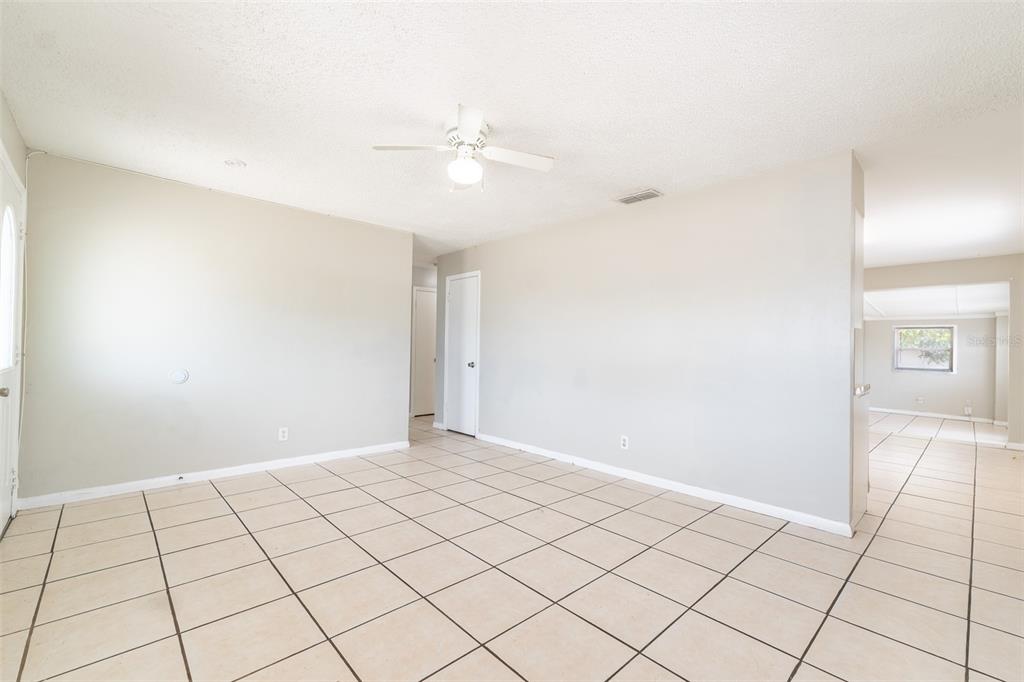 An empty living room with light-colored tile flooring, beige walls, and a ceiling fan — 6001 CRESTRIDGE ROAD, TAMPA, FL