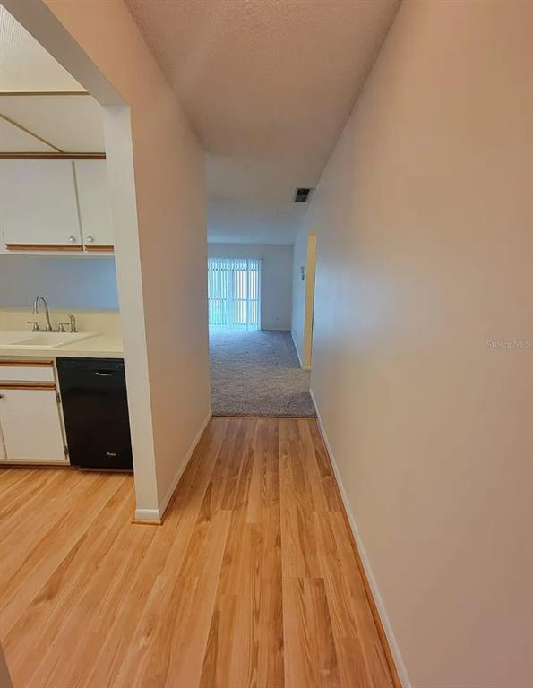 A kitchen with white cabinets and a black dishwasher opens into a carpeted living area — 100 E KENTUCKY AVE UNIT 103D, DELAND, FL