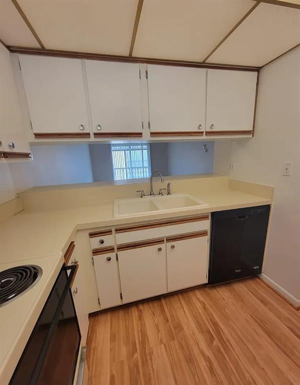 A kitchen features white cabinets with wood trim, a double sink, and a black dishwasher — 100 E KENTUCKY AVE UNIT 103D, DELAND, FL