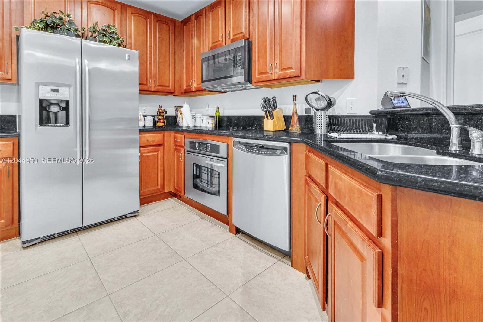 A kitchen features wooden cabinets, stainless steel appliances, and black granite countertops — 16100 Emerald Estates Dr # 298, Weston FL 33331, WESTON, FL