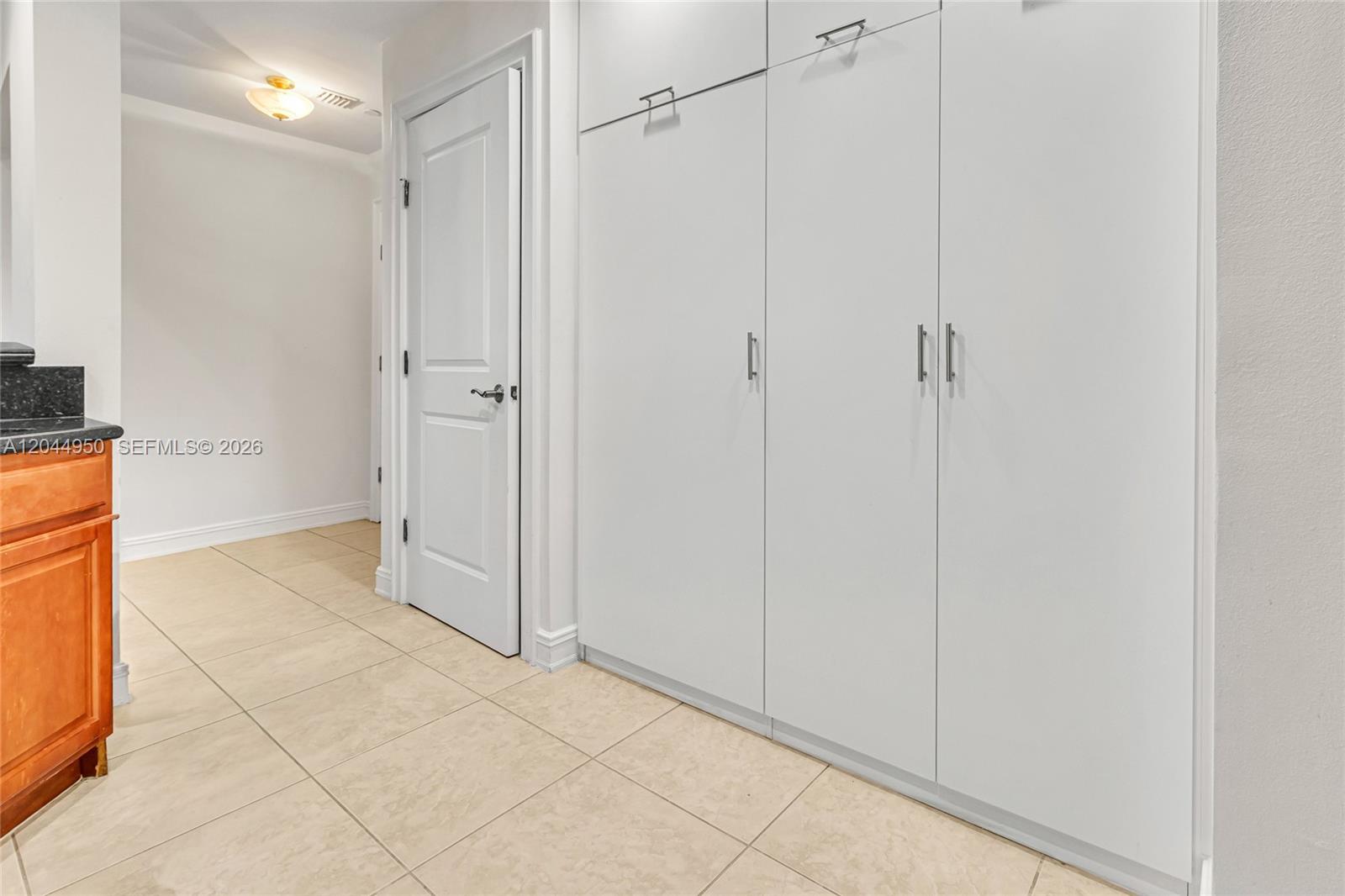 A hallway features beige tile flooring, a white door, and a wall of white cabinets — 16100 Emerald Estates Dr # 298, Weston FL 33331, WESTON, FL