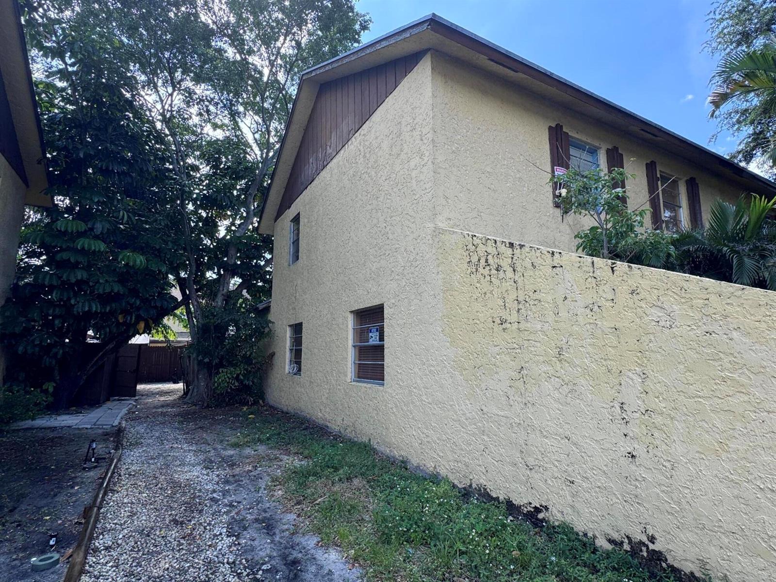 A side view of a two-story stucco building with a gravel path and mature trees — 4346 NW 4th Avenue, Deerfield Beach FL 33064, DEERFIELD BEACH, FL