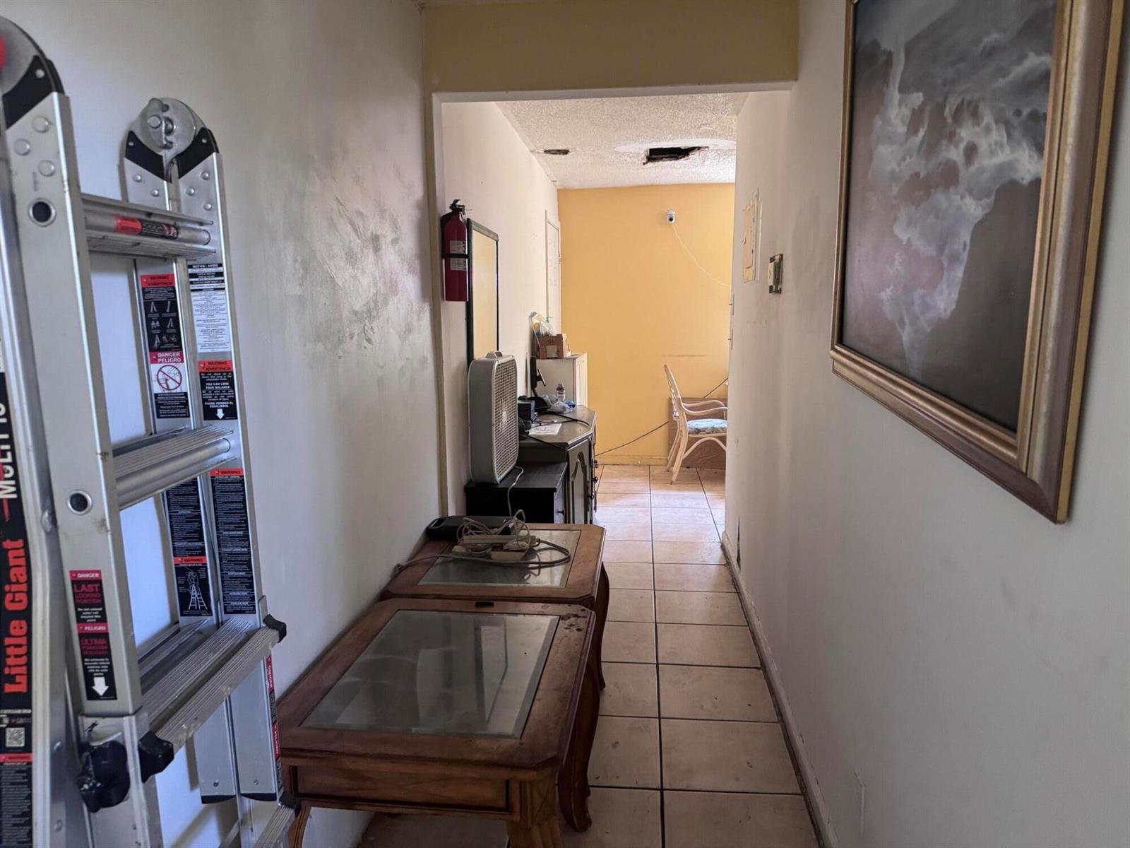 A hallway with a ladder, two glass-topped tables, and a view into a yellow room — 4346 NW 4th Avenue, Deerfield Beach FL 33064, DEERFIELD BEACH, FL