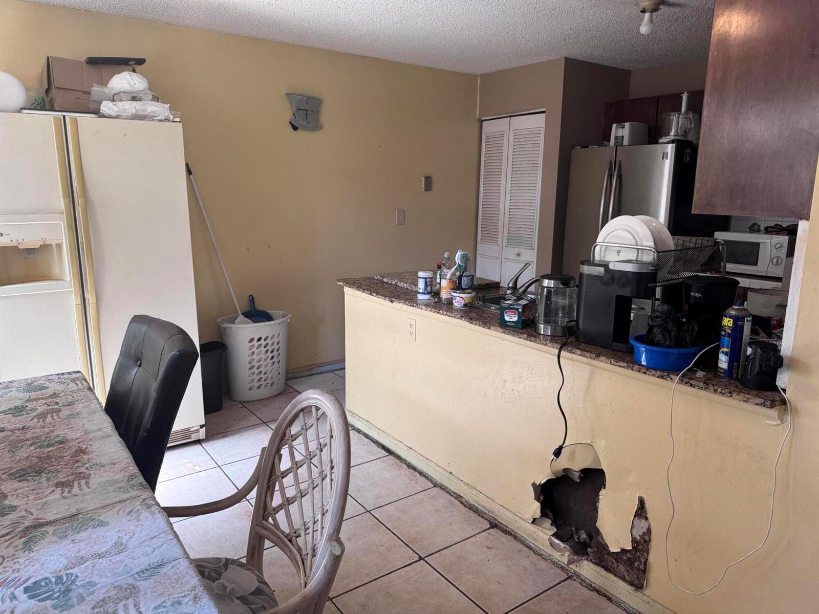 A kitchen with a damaged wall, tile flooring, a breakfast bar, and a dining area — 4346 NW 4th Avenue, Deerfield Beach FL 33064, DEERFIELD BEACH, FL