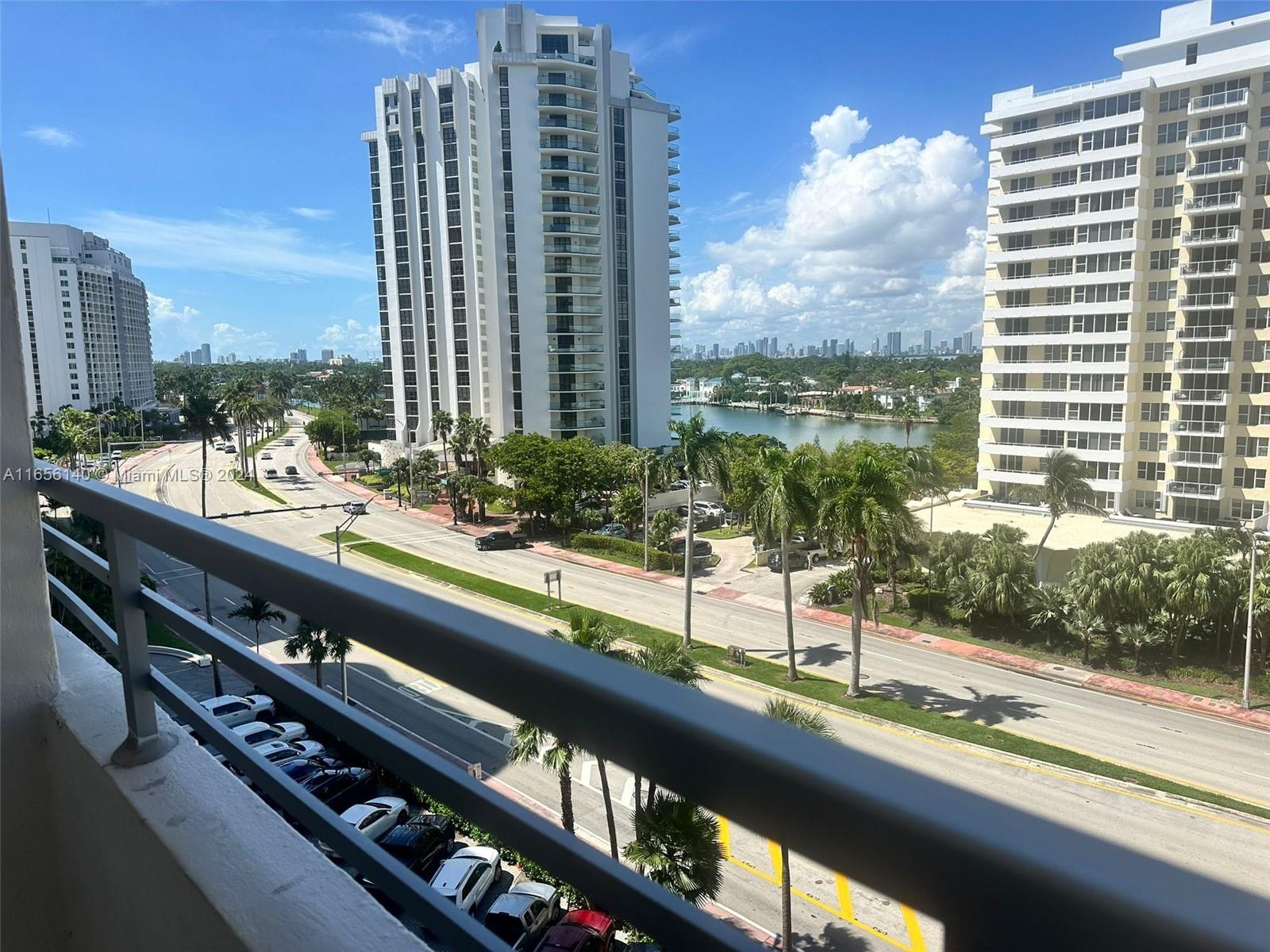A balcony view overlooking a multi-lane road, palm trees, a waterway, and several high-rise buildings — 5555 Collins Ave # 8Z, Miami Beach FL 33140, MIAMI BEACH, FL