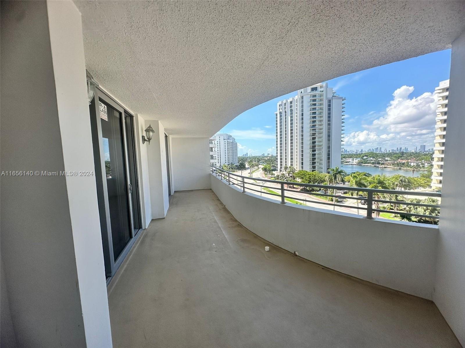 A curved balcony overlooks a waterfront cityscape with high-rise buildings and palm trees — 5555 Collins Ave # 8Z, Miami Beach FL 33140, MIAMI BEACH, FL