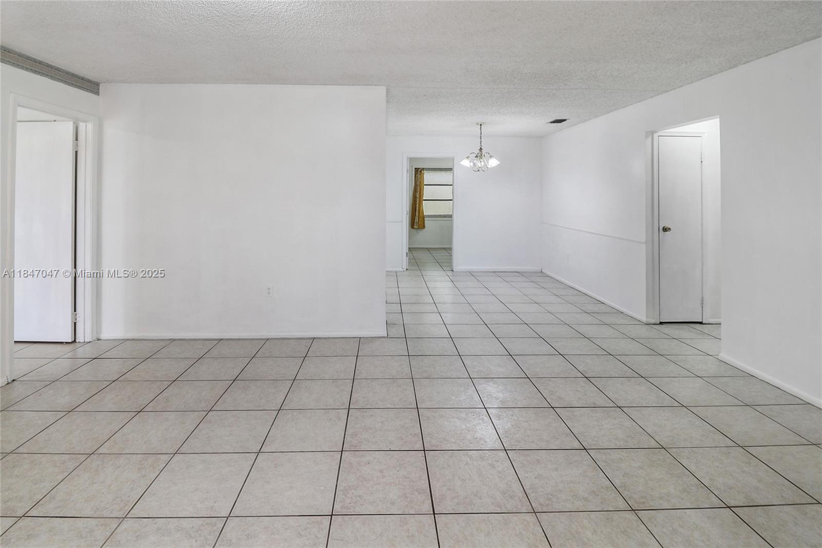 An empty room with white walls, tiled floors, and a central chandelier — 12020 NW 34th Pl, Sunrise FL 33323, SUNRISE, FL